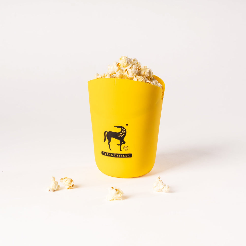 
                  
                    Front view of the yellow Terra Delyssa silicone popcorn popper with popcorn spilling out, featuring the brand’s horse logo prominently displayed.
                  
                
