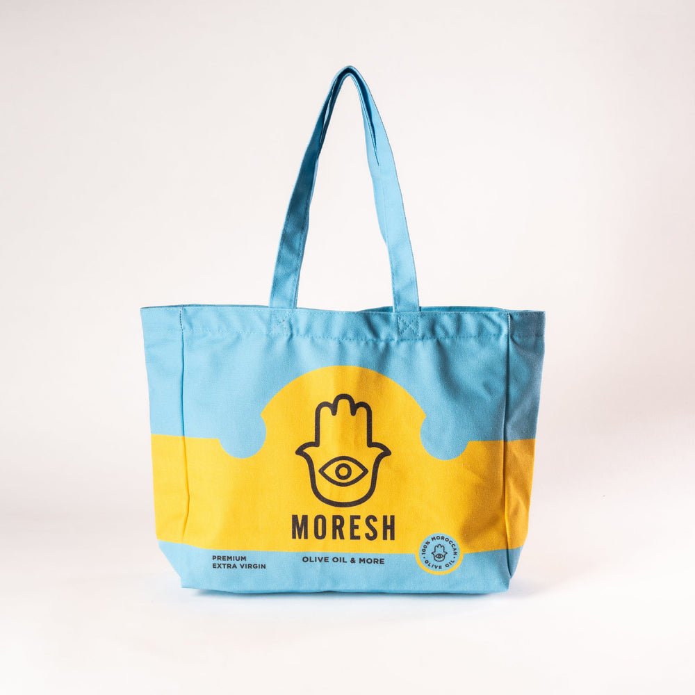 Moresh canvas tote bag in blue and yellow, made from eco-friendly fabric with minimalist branding, displayed on a neutral background.